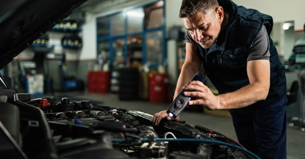 mechanic_examining_car_engine_while_using_lamp