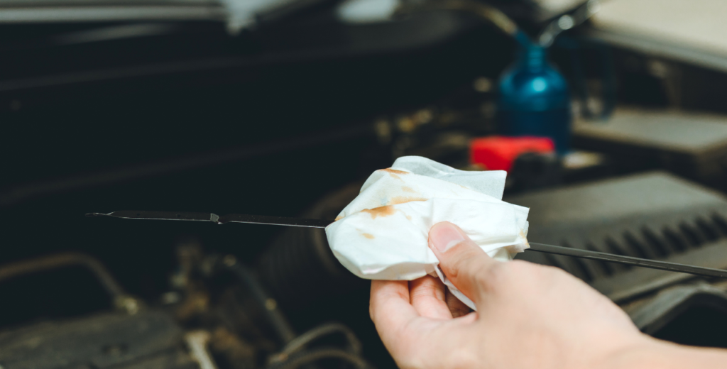 A person inspecting a car engine while holding a transmission dipstick and tissue for checking automatic transmission fluid