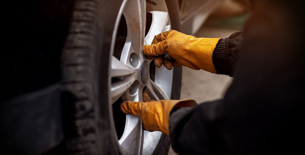 A person in gloves is changing a tire on a car, removing the wheel to access and change the brake pads.