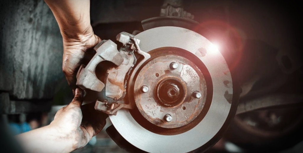 A person wearing gloves is changing a tire on a car, having removed the caliper to access the brake pads.