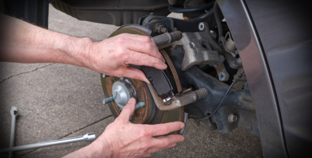 A person removes old brake pads while fixing a car's brake system, demonstrating automotive repair skills.
