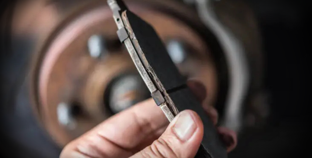 A person demonstrates the installation of new brake pads while holding one in front of a car.