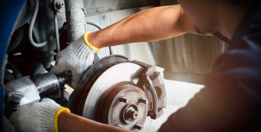 A man carefully reattaches the caliper while working on a car's brake system in a well-lit garage.