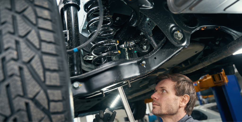 A man is inspecting a car's suspension system while working underneath the vehicle.