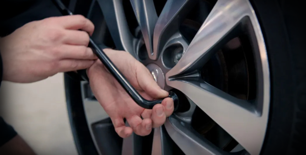 A person using a wrench to fix a tire, demonstrating the process of loosening nuts for brake pad replacement.