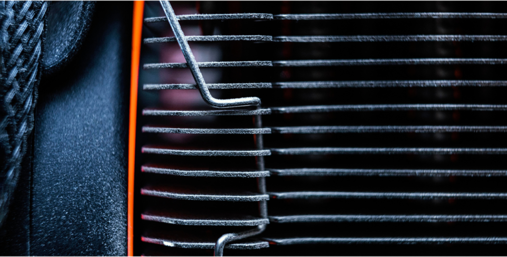 Close-up of a vehicle radiator with cooling fins and a wire clip, highlighting potential areas where leaks or damage could occur