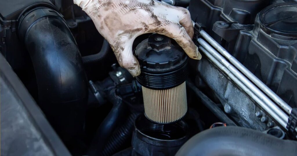 A person examining a car engine with a hose, suggesting issues with a clogged fuel filter.