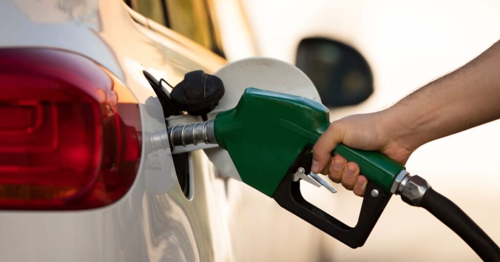 A person standing next to their car, filling the gas tank at a petrol pump.