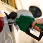 A person standing next to their car, filling the gas tank at a petrol pump.