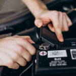 A person inspecting and working on a car battery, focusing on maintenance and replacement timing.