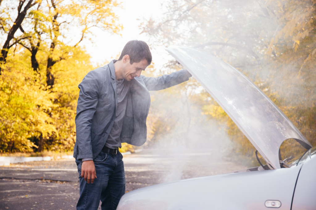 A man stands beside his car with the hood open, addressing an overheating issue.
