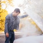 A man stands beside his car with the hood open, addressing an overheating issue.