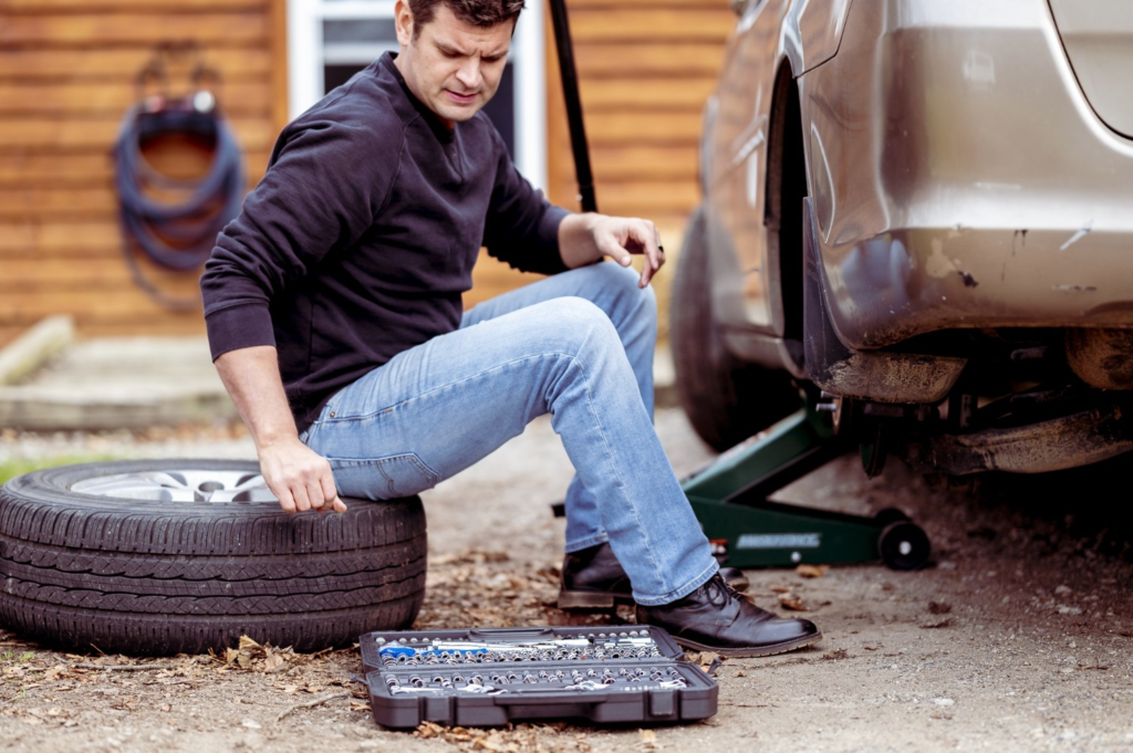 A man using a tool to fix a flat tire, demonstrating the process of changing a tire.