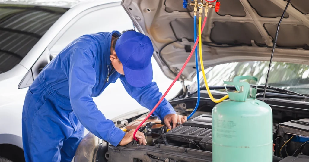 Car AC refrigerant recharge by mechanic in blue suit