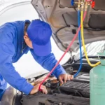 Car AC refrigerant recharge by mechanic in blue suit