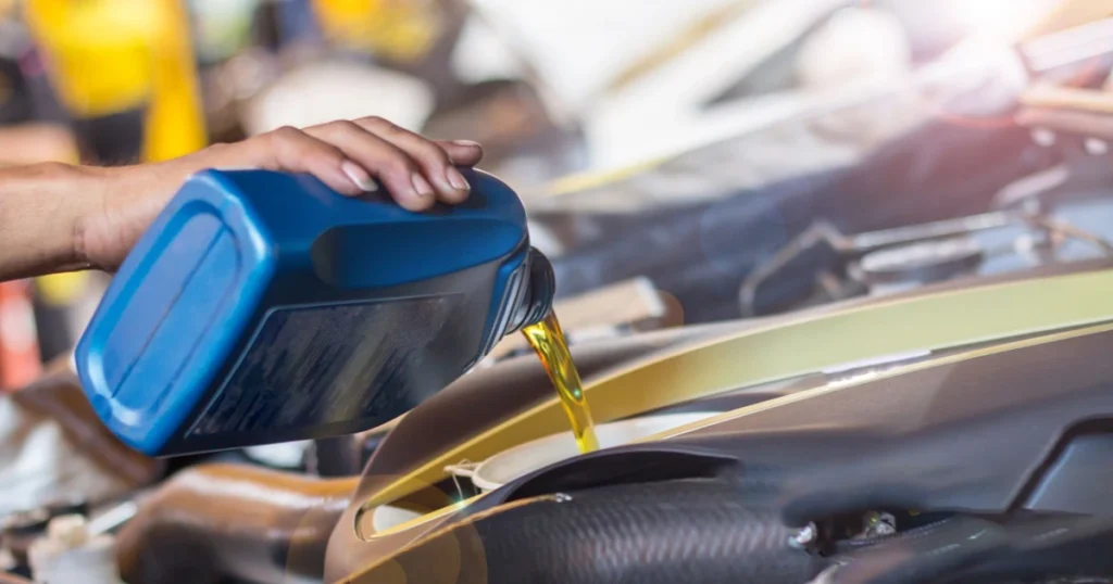 Mechanic pouring synthetic oil into a car engine during maintenance.