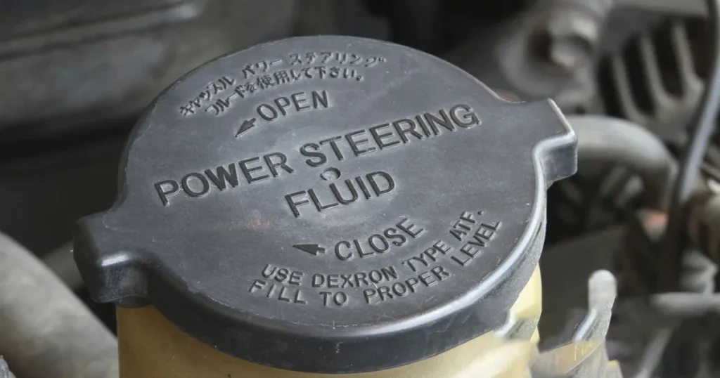 Close-up of a power steering fluid reservoir cap under a car hood.