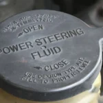 Close-up of a power steering fluid reservoir cap under a car hood.