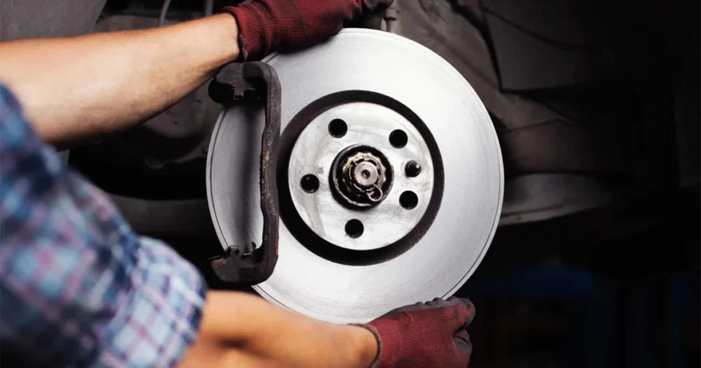 A mechanic wearing red gloves holding a clean brake rotor disc during a brake system repair.