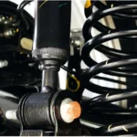 Close-up of a vehicle's suspension system showing the black coil spring and shock absorber strut.