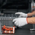 A specialist inspecting a large, multi-cell hybrid vehicle battery pack on a workbench.