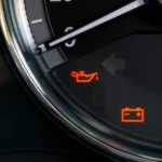 Close-up of a car dashboard showing illuminated red warning icons for low oil pressure and battery charging issues.