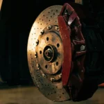 Close-up of car brake disc with red caliper in workshop.