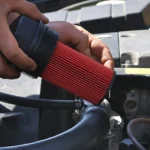 Installing a new oil filter in a car engine compartment.