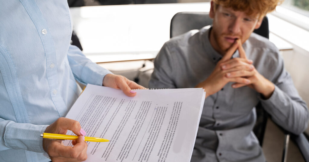 A person holds a yellow pen and a legal document toward a man who looks distressed, likely discussing accident findings.