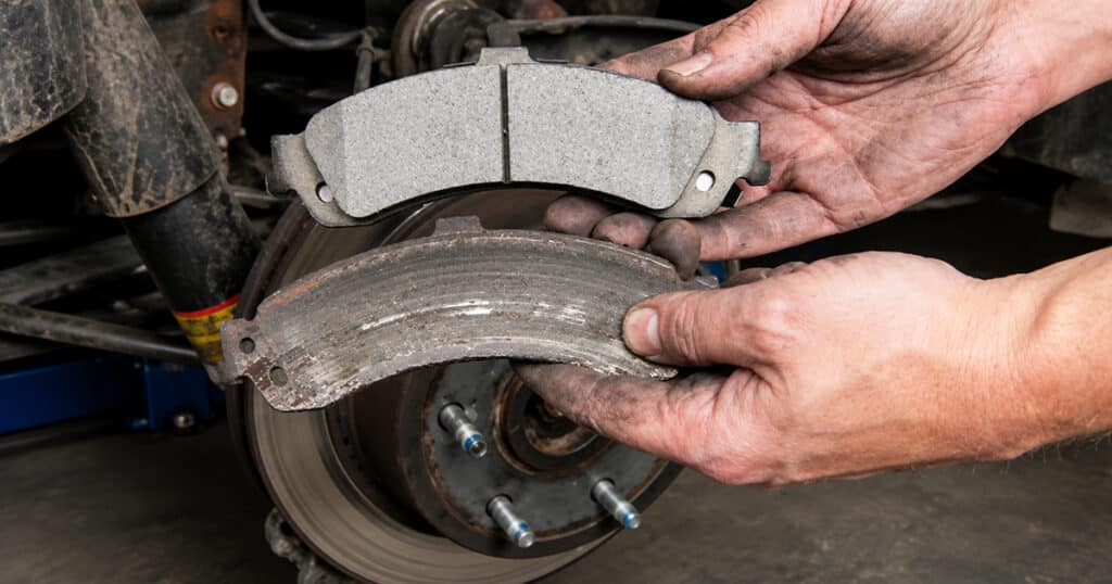 Mechanic comparing old and new brake pads near a brake rotor.