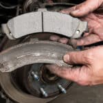 Mechanic comparing old and new brake pads near a brake rotor.
