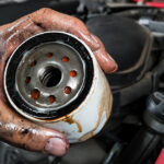 Greasy hand holding a used oil filter over a car engine.