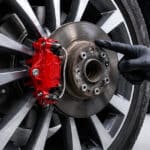 Brake rotor and red caliper being inspected by a mechanic.