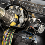 Exposed car steering column wiring and dashboard controls.