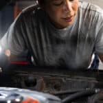 A mechanic uses a flashlight to inspect an engine under the hood of a car.