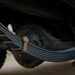 A close-up underneath a vehicle, focusing on a leaf spring suspension system attached to the rear axle.