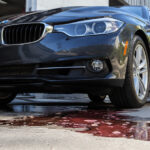 Low-angle view of a black BMW with a dark fluid leak on the concrete below