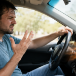 Frustrated man sitting in a car as hot air blows from the AC vents.