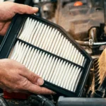 A person holding a new car air filter over an open engine compartment.