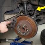 Hand pointing at a rusty brake rotor and caliper.