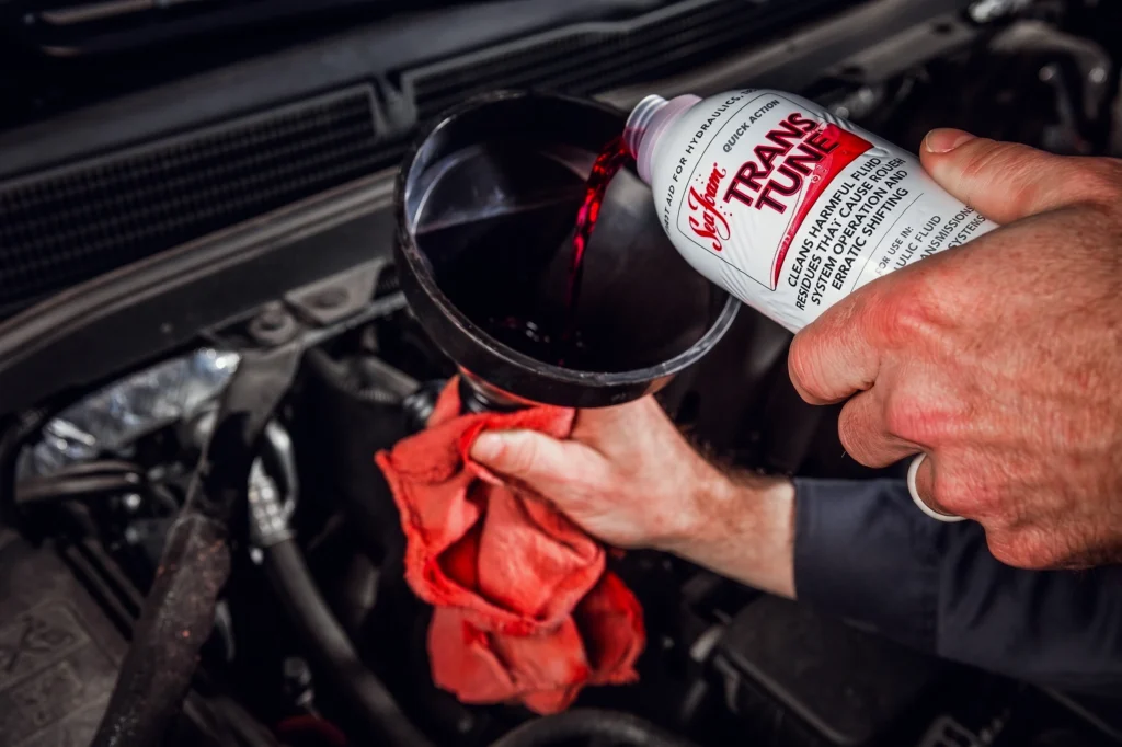 Pouring transmission additive fluid into a car engine with a funnel.