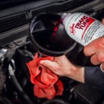 Pouring transmission additive fluid into a car engine with a funnel.