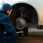A mechanic inspecting a brake master cylinder under the hood of a vehicle