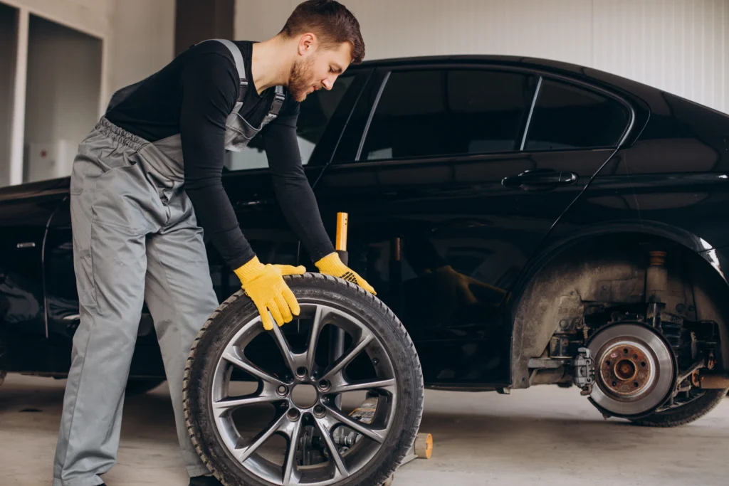 Mechanic in grey overalls replacing a wheel on a black car