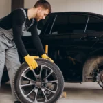 Mechanic in grey overalls replacing a wheel on a black car