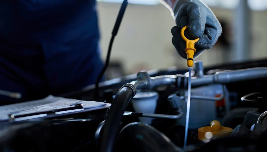 Mechanic pulling yellow dipstick to check car engine oil level.