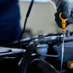 Mechanic pulling yellow dipstick to check car engine oil level.