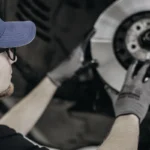 Auto technician wearing gloves inspecting front brake rotor and hub.
